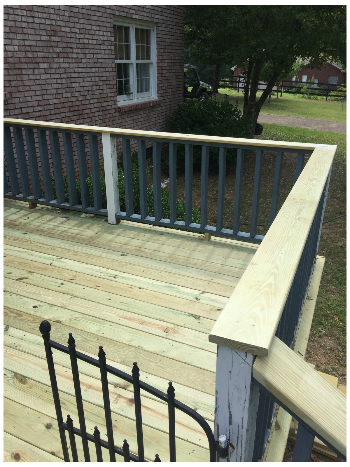 Partially finished wooden deck and railing attached to a red brick building, with a black metal gate resting on the boards