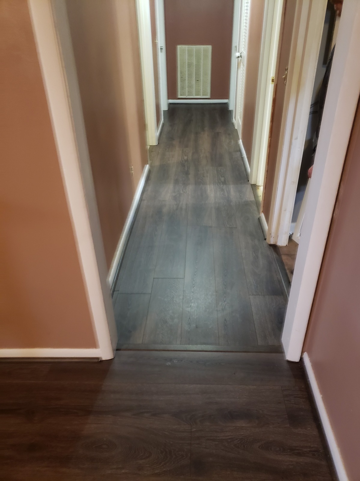 Long interior hallway with grey wood-look plank flooring, mauve walls and white trim