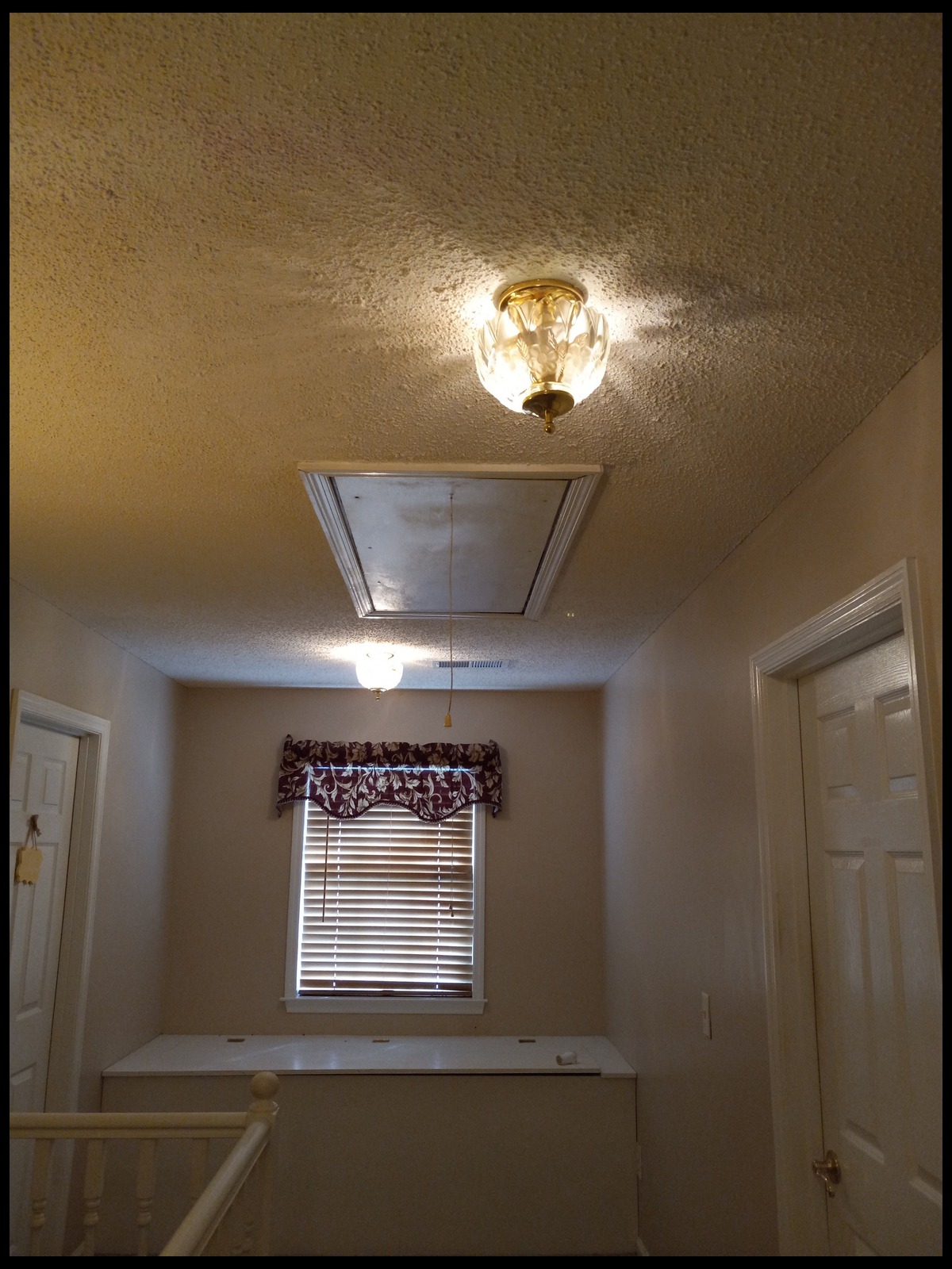 Stairwell landing with repainted beige walls and ceiling, a new glass and brass flush-mount light, and an attic access panel