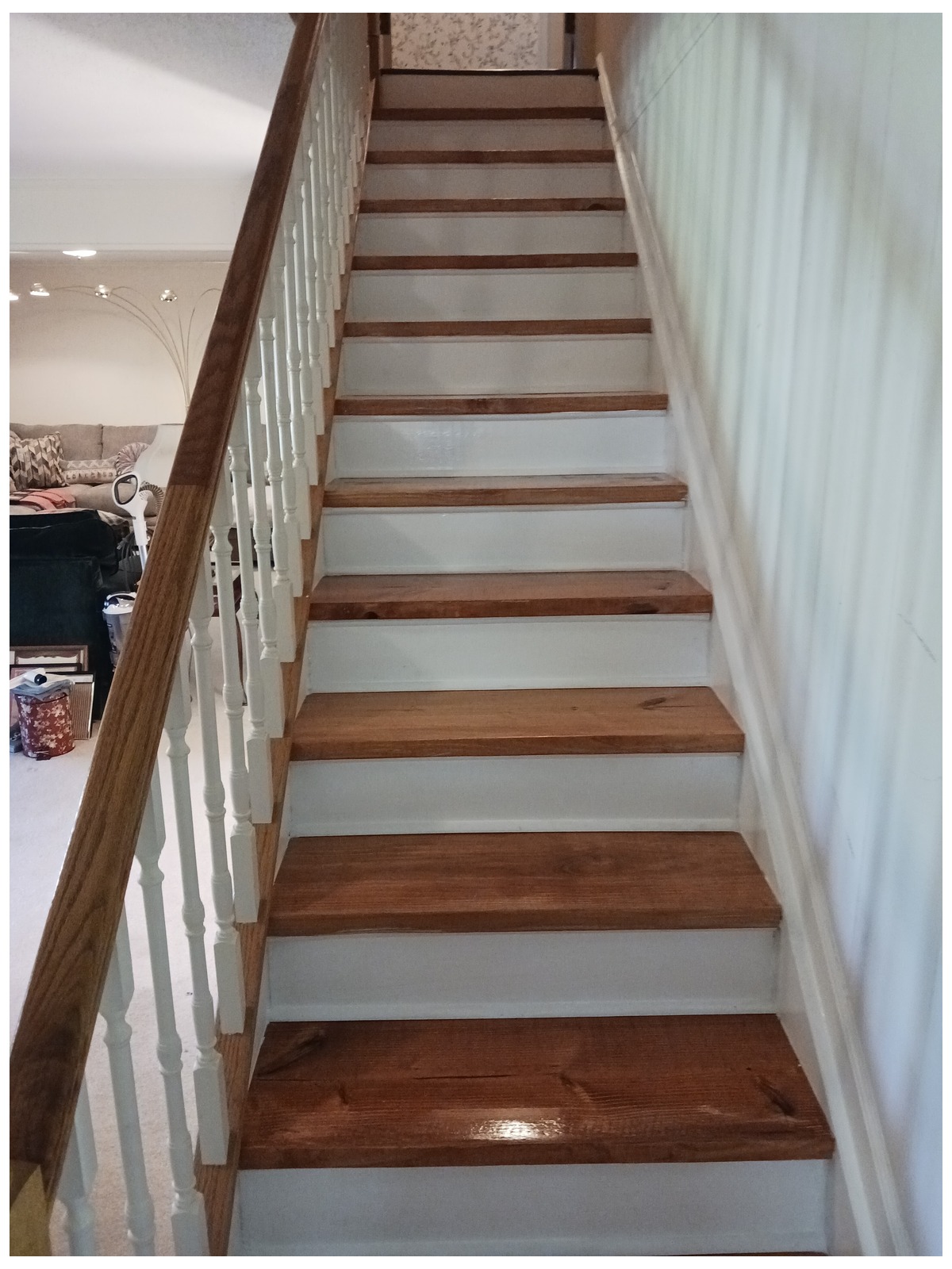 Finished straight staircase with stained wood treads and white risers, opening onto a living room
