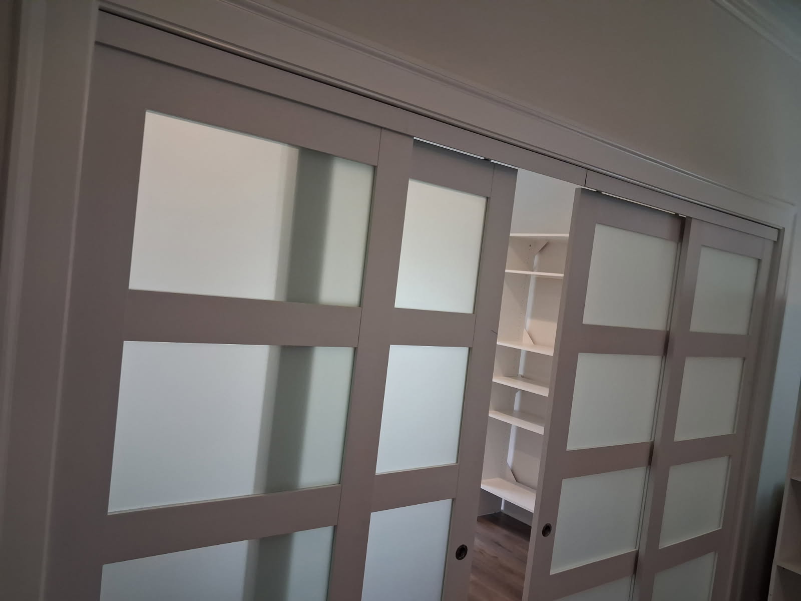 Frosted glass sliding door partly open, showing white closet shelving behind it
