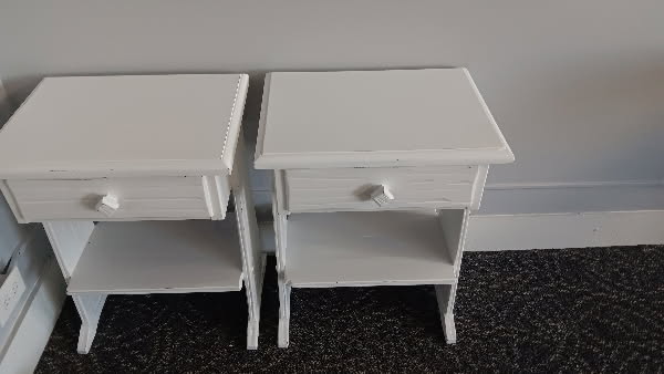 Two matching white wooden nightstands with a single drawer and an open shelf, set side by side against a gray wall