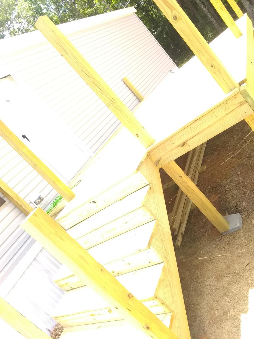 Newly built wooden staircase and landing leading up to a platform with a wooden railing, on posts set in concrete footings