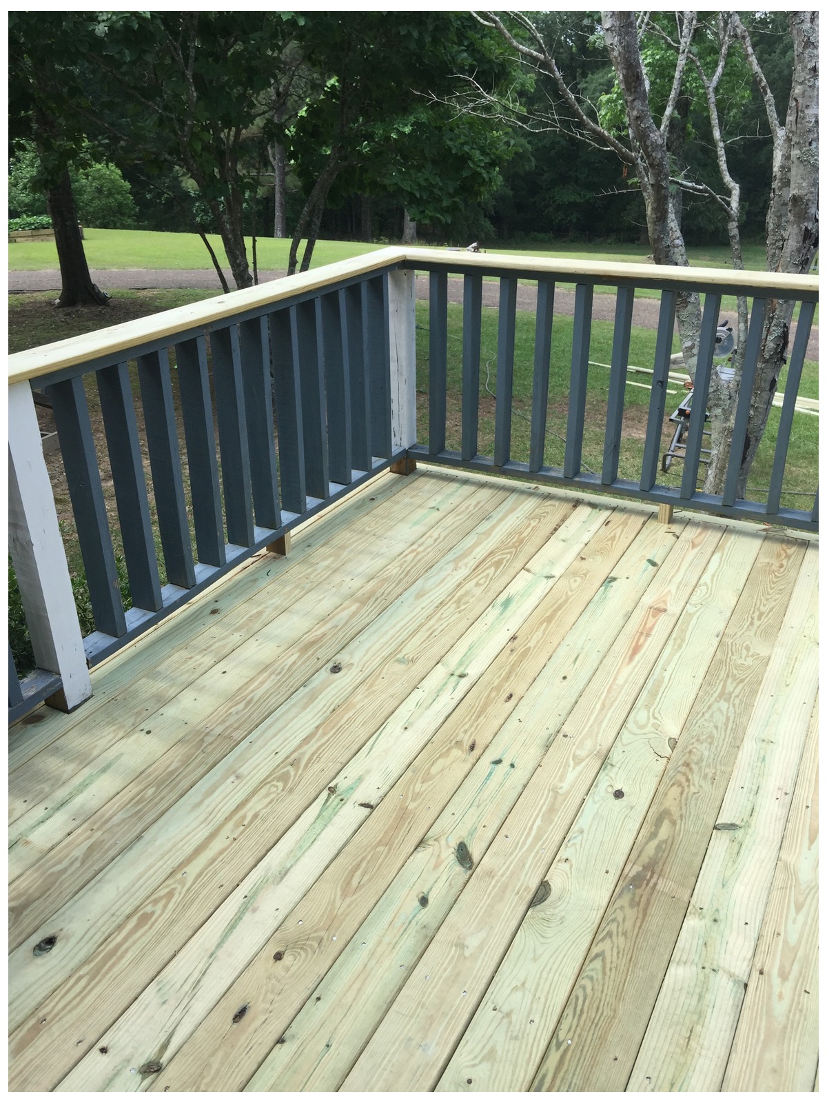 Newly built wooden deck with light pressure-treated boards and dark grey balusters under a light wood handrail