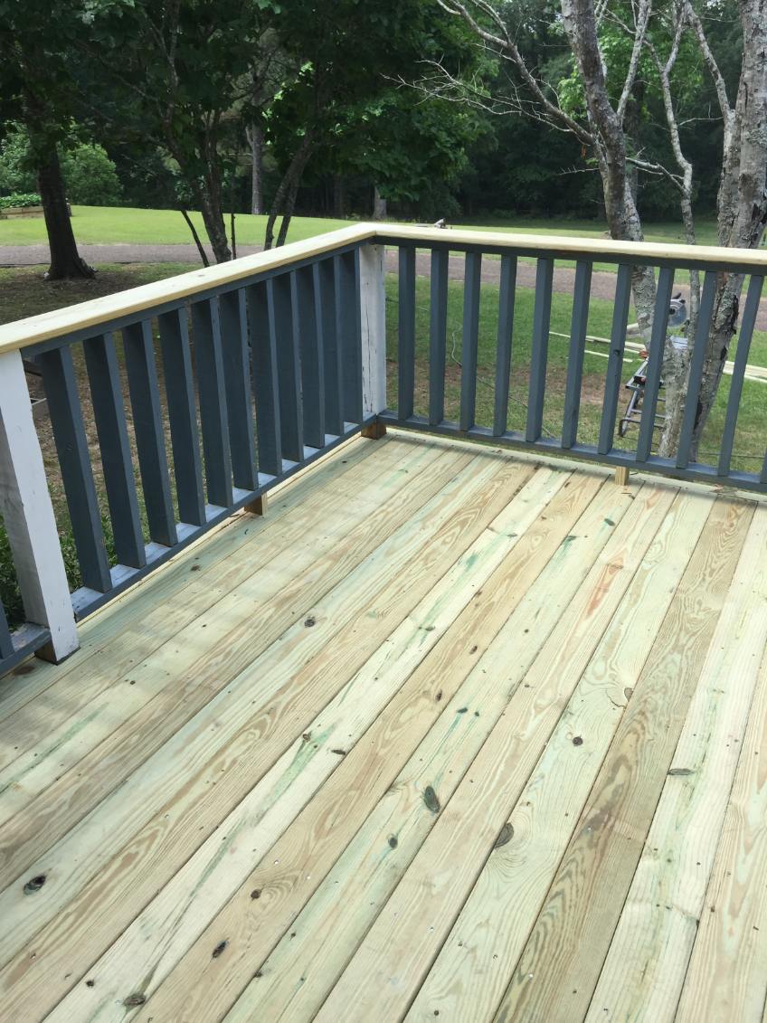 Newly built wooden deck with light pressure-treated floorboards and a railing with dark gray balusters, white posts and a light wood handrail