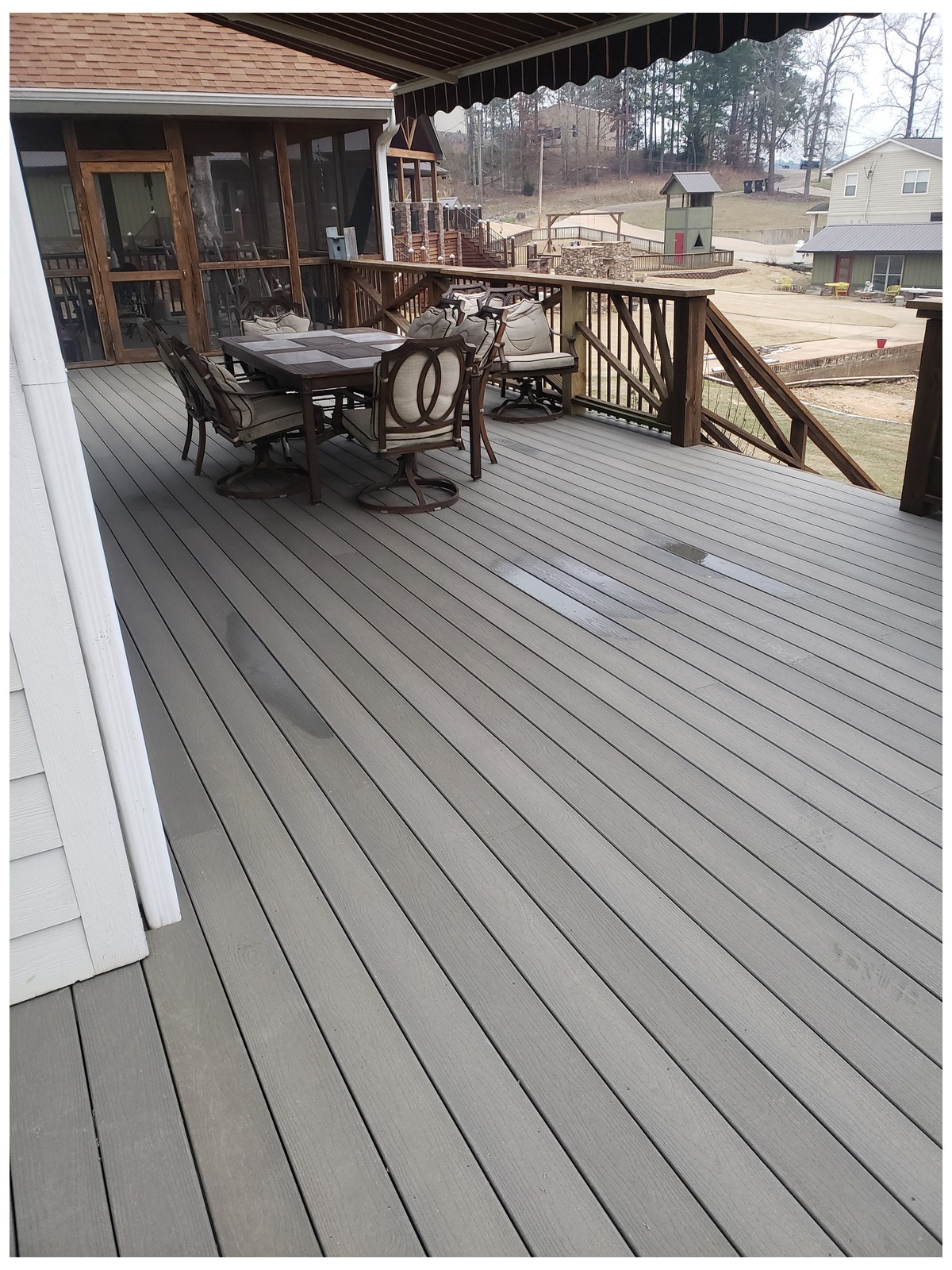 Finished grey composite deck with a wooden railing, a patio table and six chairs, attached to a house with a screened porch