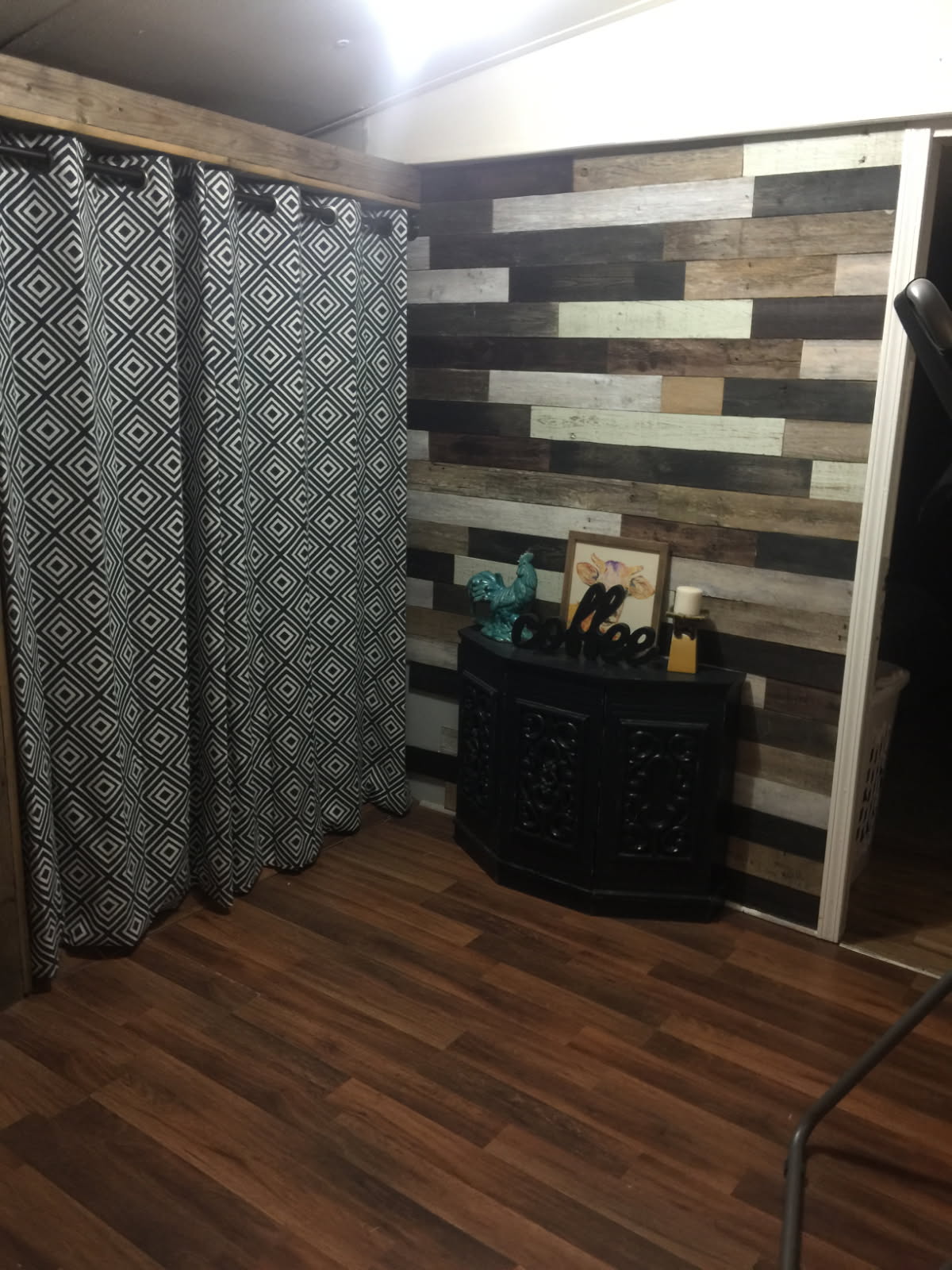 Interior corner with a wall finished in horizontal reclaimed wood boards above a dark cabinet, beside patterned floor-length curtains