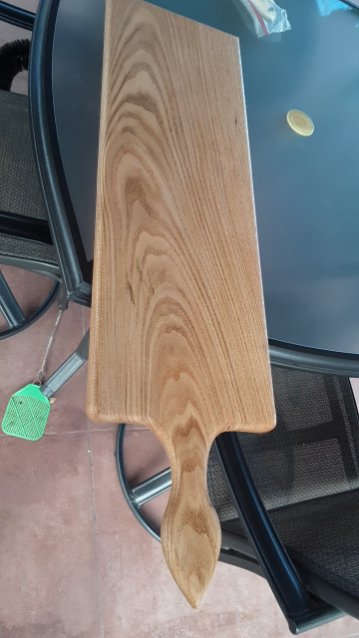 Handmade wooden serving board with a paddle handle and a strong swirling grain, resting on an outdoor table