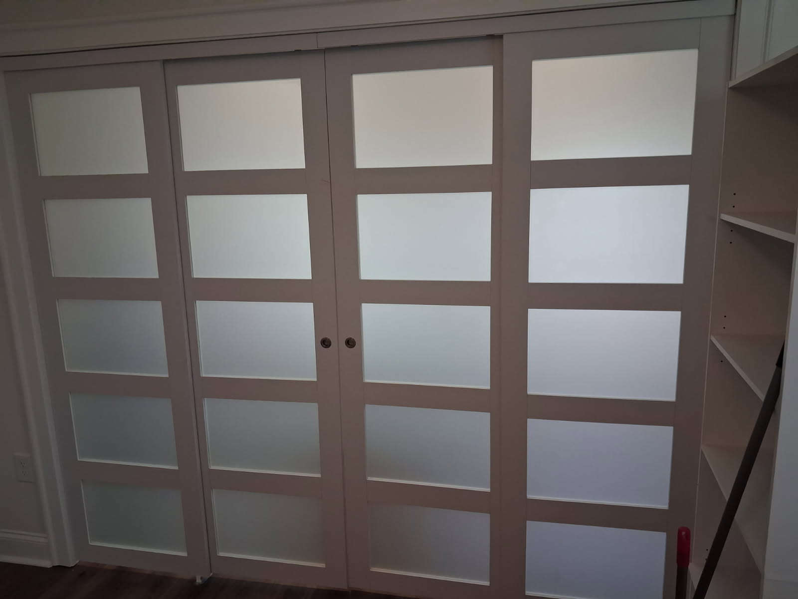 Wide four panel sliding closet door unit with frosted glass inserts, beside white built-in shelving