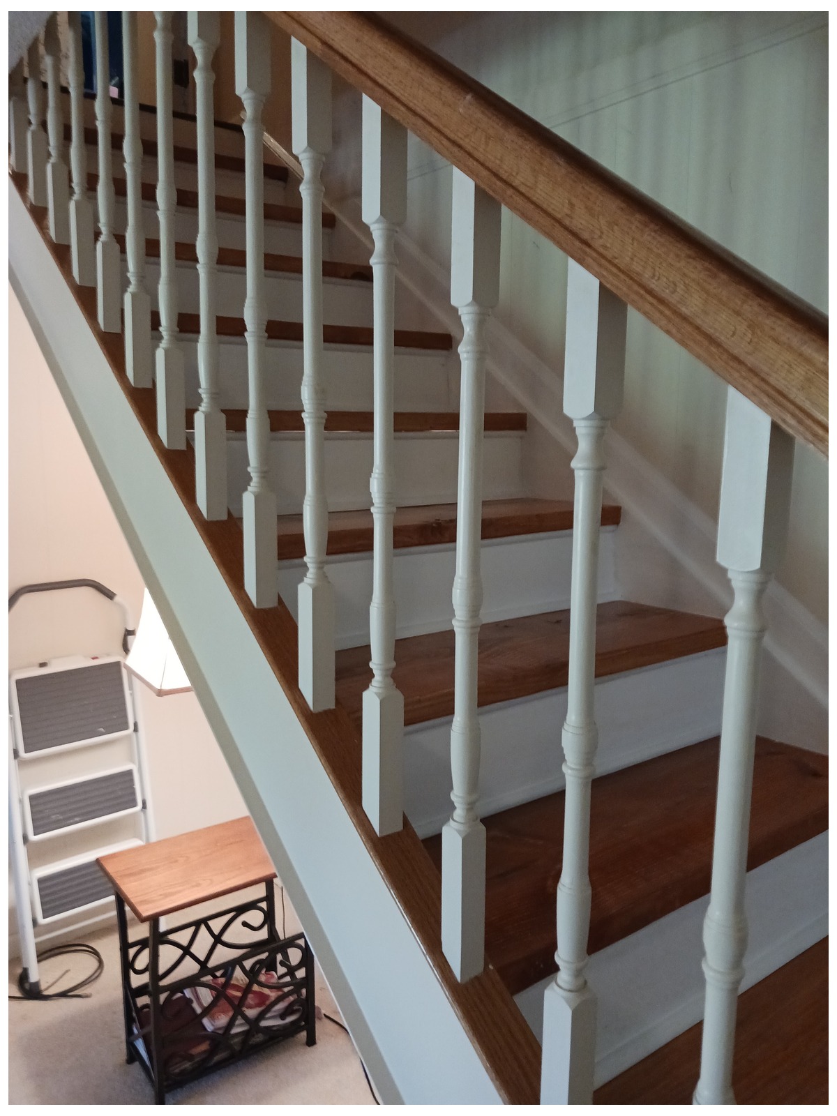Staircase seen from below with a wood handrail and white turned balusters against white walls