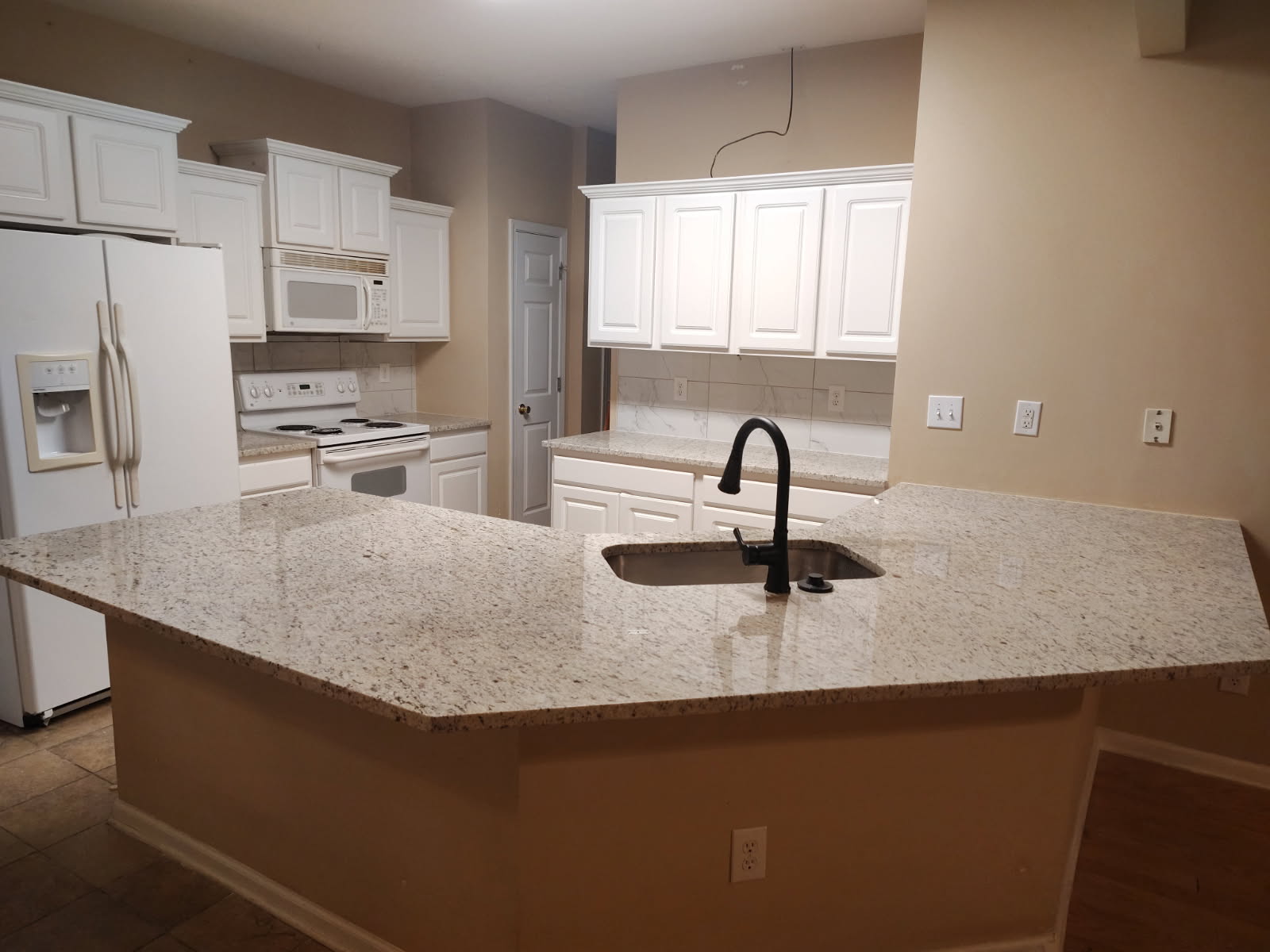 Finished kitchen with white cabinetry, a center island with a speckled granite top and an undermount sink with a black faucet