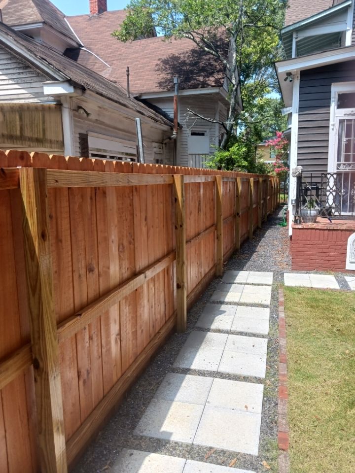 Wooden privacy fence along a narrow side yard with a paver walkway leading to a brick porch